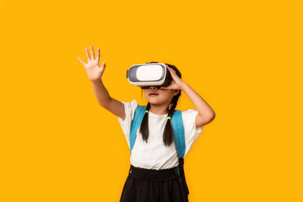 istock Asian Schoolgirl Wearing Virtual Reality Glasses Standing Over Yellow Background 1264242529