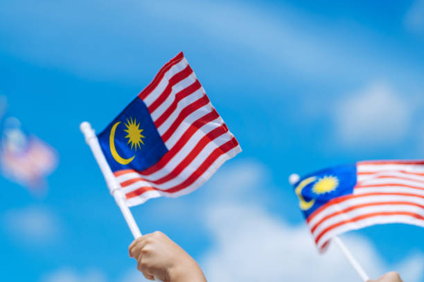 istock Hand happily waving Malaysia flag against blue sky. 1264242729