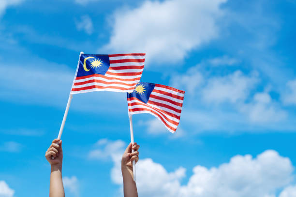 istock Hand happily waving Malaysia flag against blue sky. 1264242798