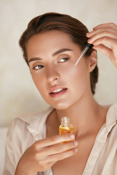 Beauty Face. Woman Applying Essential Oil On Facial Skin And Looking Away. Beautiful Model Moisturizing Derma With Natural Vitamin E, Serum Collagen And Hyaluronic Acid. Beauty Face. Woman Applying Essential Oil On Facial Skin And Looking Away. Beautiful Model Moisturizing Derma With Natural Vitamin E, Serum Collagen And Hyaluronic Acid. electromagnetic photos stock pictures, royalty-free photos & images