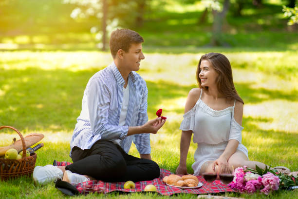 Young man making proposal to his girlfriend, giving her engagement ring at park