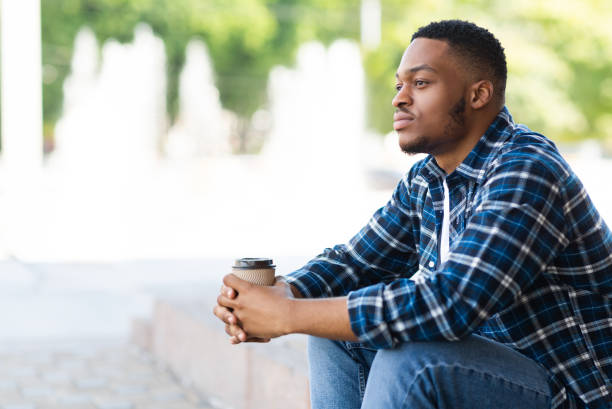 Portrait of pensive african american guy sitting with coffee Side view of pensive african american person sitting in the park with coffee, looking aside, free space soul searching stock pictures, royalty-free photos & images