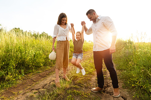 Upbringing. Lovely parents spending time with their child who is jumping up on the road