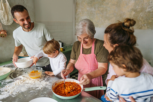 Photo of a happy multigenerational family making pasta in the kitchen; having a great time while making food and enjoying each other's company.