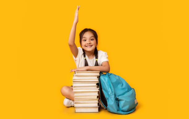 istock School Girl Raising Hand Sitting At Book Stack, Studio Shot 1264247168