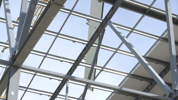 istock Modern storehouse construction site, structural steel structure of new commercial building against. Construction of modern factory or warehouse. Crane lowers roofing. Man working on roof 1264248417