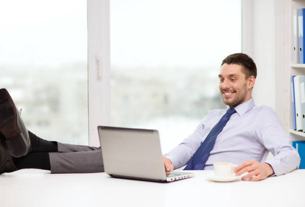 smiling businessman or student with laptop office, business, education, technology and internet concept - smiling businessman or student with laptop computer and coffee at office legs crossed at ankle stock pictures, royalty-free photos & images