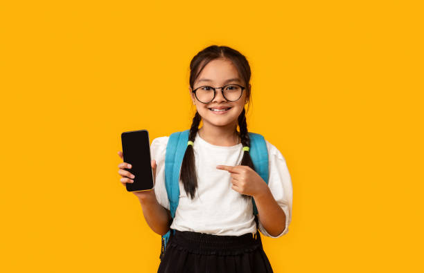 istock Asian Schoolgirl Showing Smartphone Empty Screen Over Yellow Studio Background 1264253841