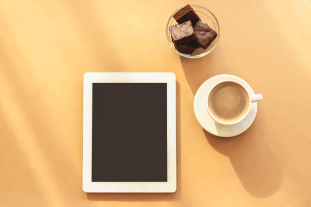 Notebook, coffee cup and chocolate cake. Cosy workplace, work at home concept. Light orange background, top view, flat lay