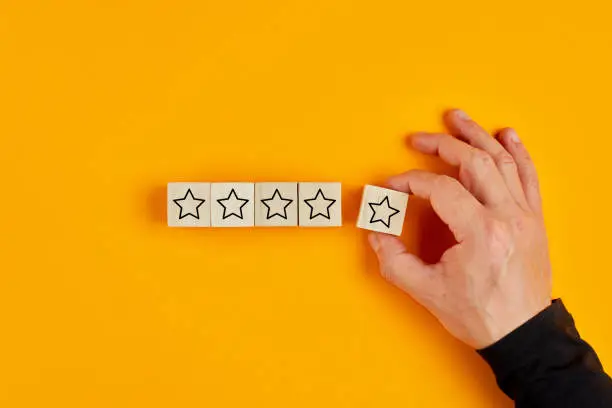 Photo of Male hand placing wooden cubes with five star rating on yellow background.  Customer satisfaction survey concept.
