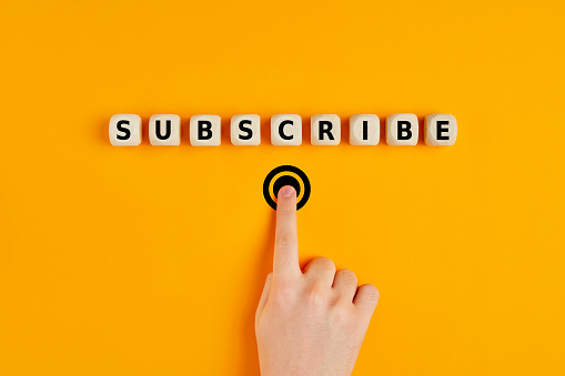 Male hand pressing subscription button with the word subscribe written on wooden blocks. Concept of online registration.
