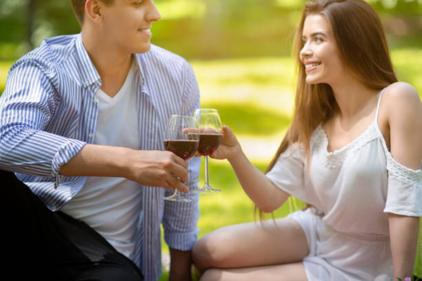 istock Young couple drinking red wine at park, focus on glasses with beverage 1264257820