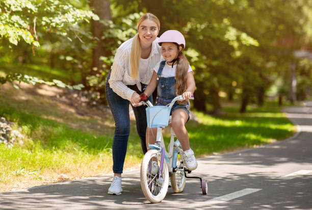 istock Mom Teaching Daughter To Ride Bicycle Spending Day In Park 1264258023