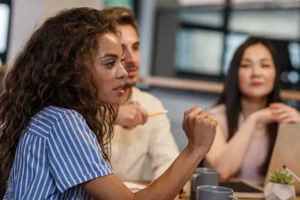 Side view of a group of multicultural entrepreneurs having a business meeting in a shared office space. Curly young woman lead the conference.