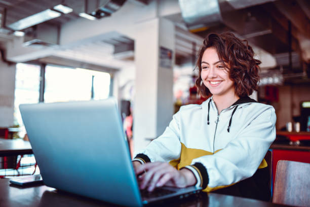 rapporto della scuola di scrittura femminile sorridente su laptop - people joy relaxation concentration foto e immagini stock