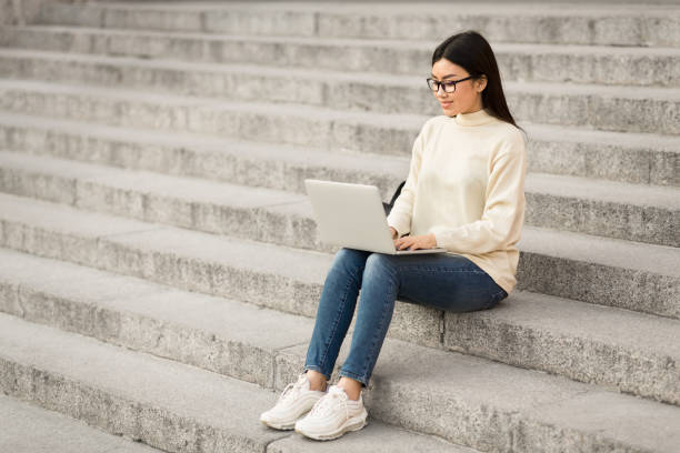 istock Woman in specs using laptop, sitting on stairs 1264269940