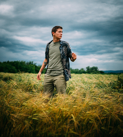 Photo of a young man, in the middle of a wheat field, looking in the stormy sky