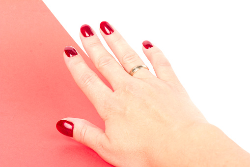 Close-up of a young woman's hands with a dark red manicure on her nails on white and red background