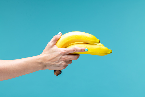 Female hand holding bunch of bananas isolated on blue background, front view. Vitamin attack.