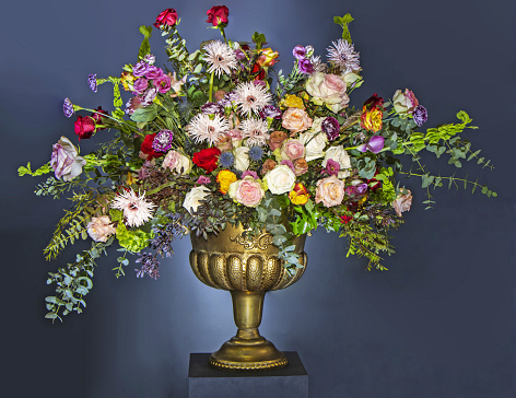 A Beautiful large flower bouquet with a lot of different flowers in a golden pot, on a blue background