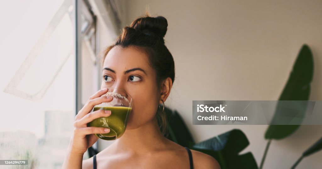 Bon appetit to healthy living Shot of a young woman drinking a green juice at home Detox Stock Photo