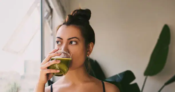 Shot of a young woman drinking a green juice at home