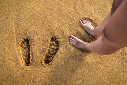 women's feet and footprints on the yellow beach sand