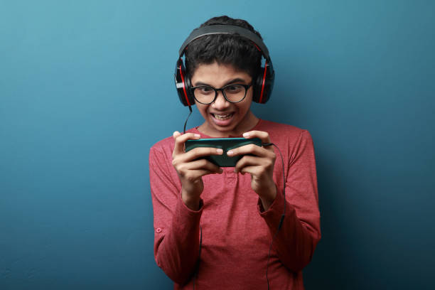 junge trägt kopfhörer spielt spiele in einem smartphone - portable player stock-fotos und bilder