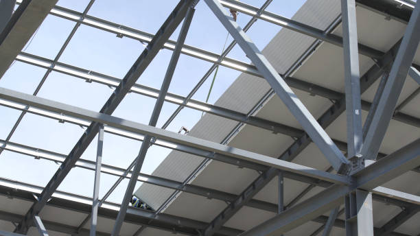 istock Modern storehouse construction site, structural steel structure of new commercial building against. Construction of modern factory or warehouse. Crane lowers roofing. Man working on roof 1264300360