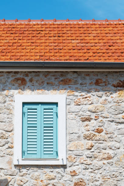 Closed window with turquoise window blinds on an old Mediterranean house with stone wall. Architecture, travel, tourism and vacation concepts.