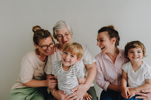 Portrait of a smiling senior woman, her daughters, and grandsons over the gray background; studio shot.