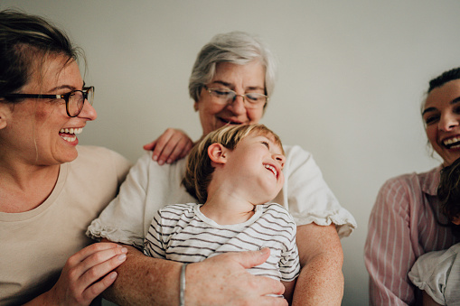 Portrait of a smiling senior woman, her daughters, and grandsons over the gray background; studio shot.