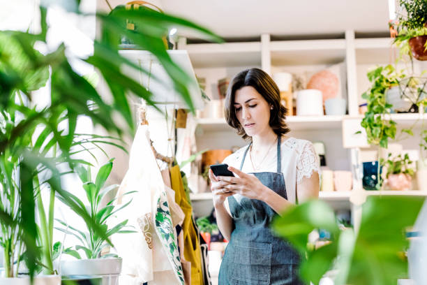 shop owner checking messages from a smart phone - boutique owner store retail occupation imagens e fotografias de stock