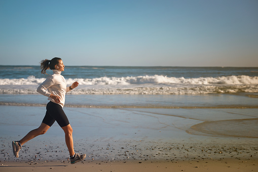 Scenic side portrait of woman running by the beach listening to music with wireless AirPods