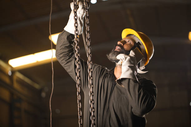 istock Male worker adjusting chain hoist while busy on phone at industry 1264315170