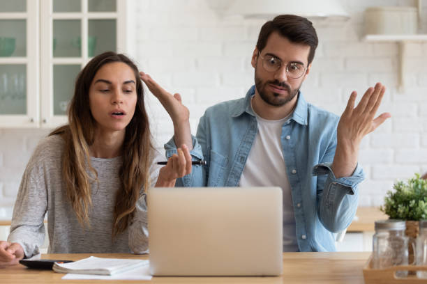Mad young couple pay online bills have laptop problems Mad young husband and wife sit at desk in kitchen feel frustrated with slow Internet connection on computer, angry millennial couple manage household finances get operational problem on laptop unusual couple stock pictures, royalty-free photos & images