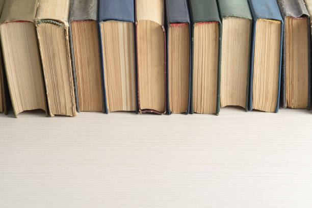 a row of old, faded, multicolored, yellowed books on a light background. - library book shelf generic imagens e fotografias de stock