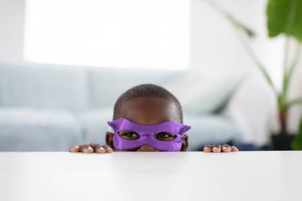 Little African boy wearing superhero mask peeks over table top