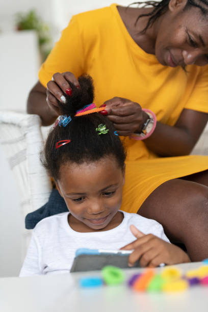 istock Mom does daughters hair while she watches digital tablet screen 1264327303