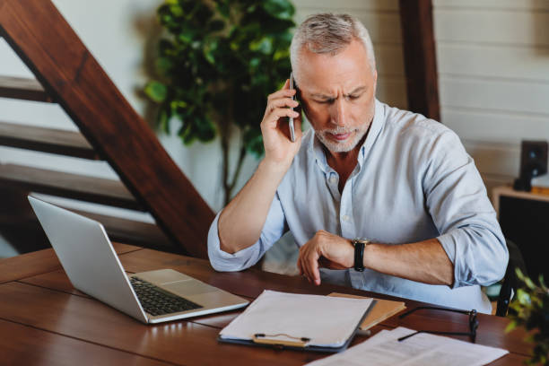 istock Man checking time. Senior man checking time on his watch at home office while talking on mobile phone 1264327673