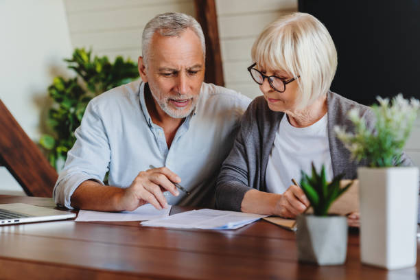 Mature couple with financial documents in home interior Mature couple with financial documents in home interior pension photos stock pictures, royalty-free photos & images