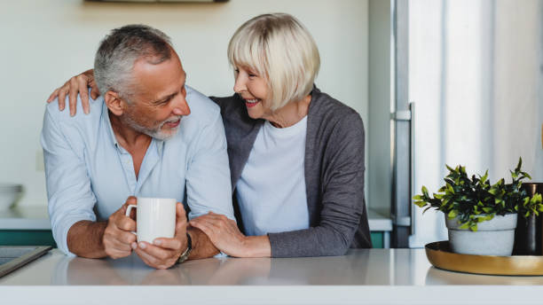istock Mature woman hugging her husband at home kitchen while he drinking coffee 1264328309