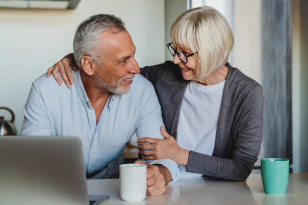 istock Senior couple hugging and using laptop in kitchen at home 1264328310