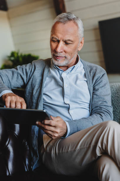 istock Vertical shot of senior man sitting on couch and using tablet pc at home 1264328321