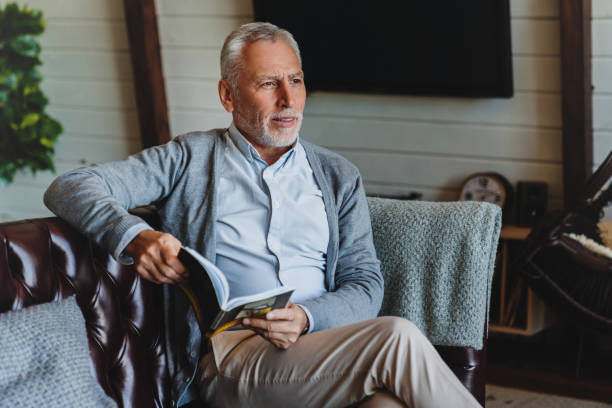 istock Senior man sitting on sofa and reading book 1264328323