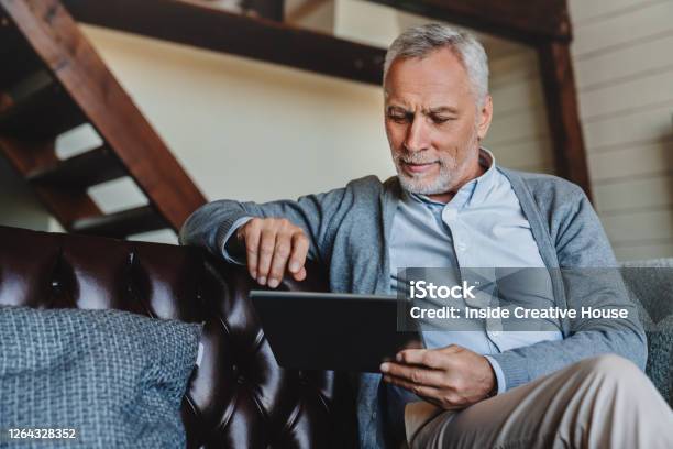 Mature Caucasian Man Websurfing On Digital Tablet At Home Stock Photo - Download Image Now