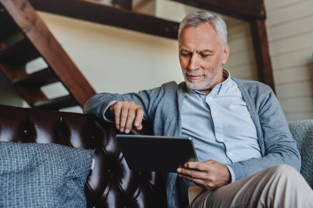 dojrzały kaukaski mężczyzna websurfing na cyfrowym tablecie w domu - ipad senior adult 70s adult zdjęcia i obrazy z banku zdjęć