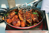 Image of metal tongs turning crispy, fried fish in a frying pan on hotplate, Goan fish curry recipe