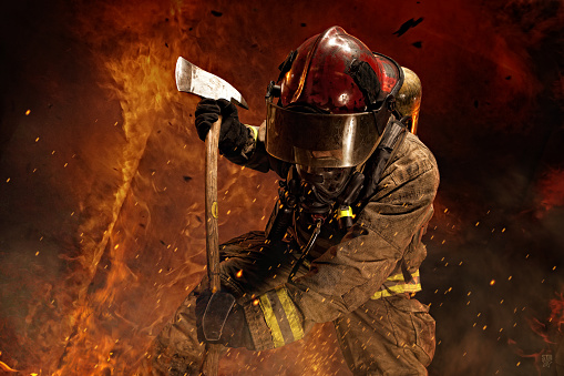 Firefighter surrounded by flames battles a fire while using an axe.