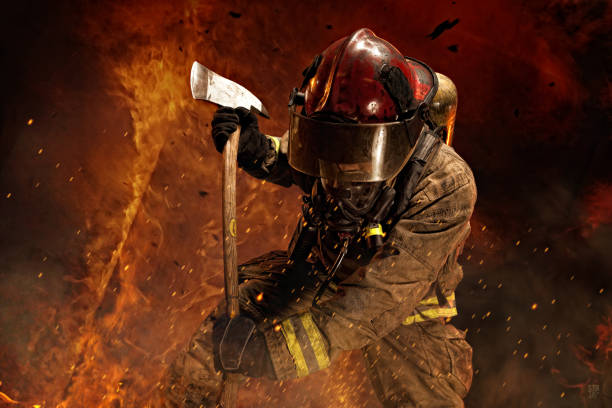 Brave Firefighter Battles Fire Firefighter surrounded by flames battles a fire while using an axe. axe photos stock pictures, royalty-free photos & images